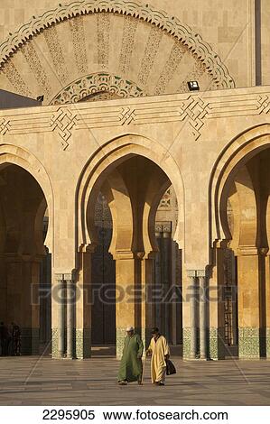 Stock Photography - Morocco, Two men walking across courtyard in front of Hassan II mosque at dusk; Casablanca. Fotosearch