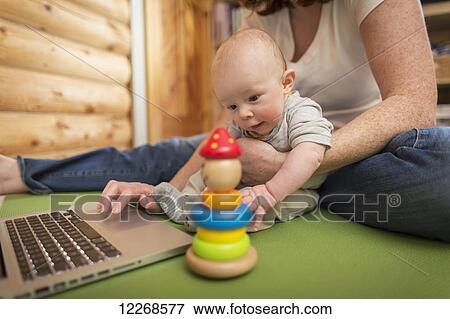 Stock Photo - Mother and baby sitting in front of a laptop on the floor of a cabin, Homer, Southcentral Alaska. Fotosearch