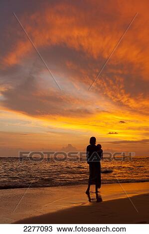 Stock Image - Mother and baby watching sunset on beach, near Unawatuna; Thalpe, Sri Lanka. Fotosearch