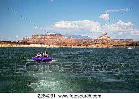 Stock Image - Mother and daughter ride on purple towable tube behind speedboat on lake powell; page arizona usa. Fotosearch