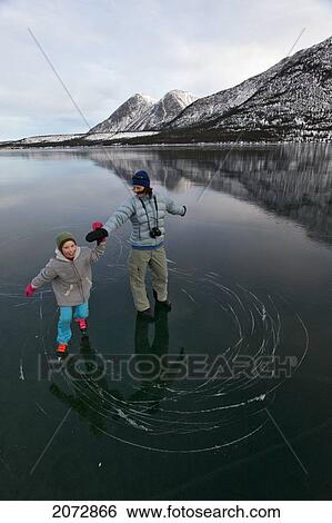 Stock Photograph - Mother And Daughter Skating On Frozen Lake In Winter, Kusawa Lake Territorial Park, Yukon, Canada. Fotosearch