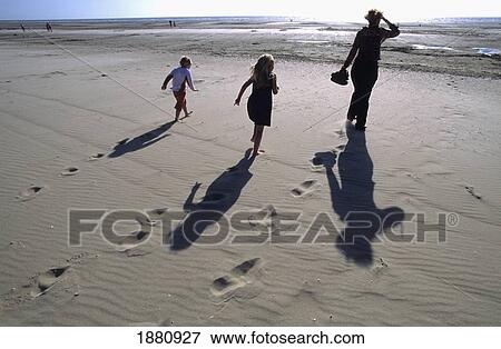 Stock Photo - Mother And Her Children Walking Barefooted On The Beach Into The Sun; Le Touquet, France. Fotosearch