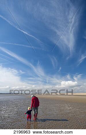 Stock Image - Mother & Child Walking Along Camber Sands At Low Tide, East Sussex, England.. Fotosearch