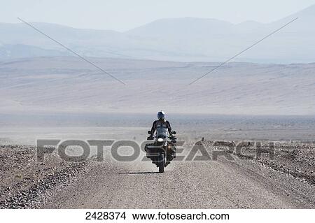 Picture - Motorcycle and rider on an arid stretch of road in a remote area; Andes, Chile. Fotosearch