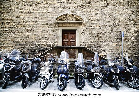 Stock Photo - Motorcycles parked in a row outside the entrance to a stone building; Florence, Tuscany, Italy. Fotosearch