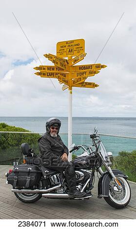 Motorcyclist sits at a destination sign on the water's edge; Bluff, South Island, New Zealand View Large Photo Image Stock Image - Motorcyclist sits at a destination sign on the water's edge; Bluff, South Island, New Zealand. Fotosearch