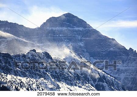 Stock Photo - Mountain Peaks With Blowing Snow Over Ridges And Blue Sky; Waterton Alberta Canada. Fotosearch
