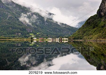 Stock Photo - Mountains And Clouds Reflected In The Tranquil Water Of Granvinsvatnet With Houses Along The Water's Edge; Granvin Hordaland Norway. Fotosearch