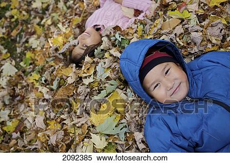 Stock Photography - Multi-Ethnic Children Lying In Autumn Leaves Outside Esl School; Guelph Ontario Canada. Fotosearch