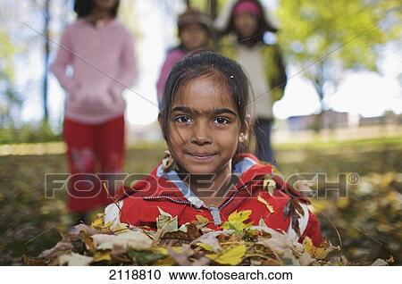 Stock Image - Multi-Ethnic New Canadian Children Playing In Autumn Leaves Outside Esl School; Guelph Ontario Canada. Fotosearch