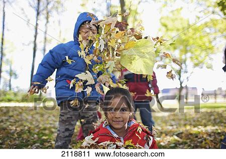 Stock Image - Multi-Ethnic New Canadian Children Playing In Autumn Leaves Outside Esl School; Guelph Ontario Canada. Fotosearch