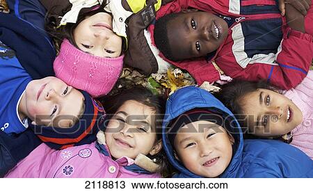 Stock Image - Multi-Ethnic New Canadian Children Lying In Autumn Leaves Outside Esl School; Guelph Ontario Canada. Fotosearch