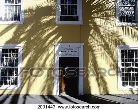 Stock Image - Muslim Man Standing In Shadow Of Palm Tree In The Door Of The Palm Tree Mosque, Long Street, Cape Town, South Africa.. Fotosearch