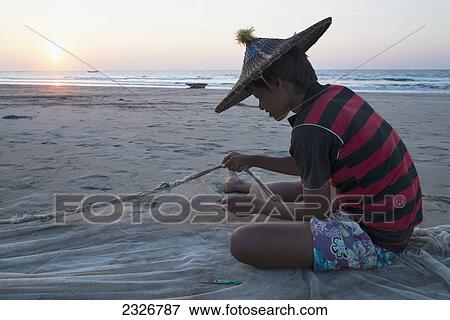 Stock Photo - Myanmar (Burma), Irrawaddyi division, Young man fixing fishing net on beach at sunset; Yea Thoe village. Fotosearch