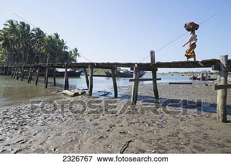 Stock Photo - Myanmar (Burma), Woman with load on her head crossing wooden bridge; Irrawaddyi division. Fotosearch