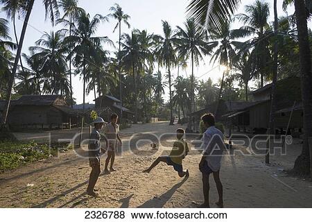 Stock Photo - Myanmar (Burma), Young men playing with ball in streets of Yea Thoe village at sunset; Irrawaddyi division. Fotosearch