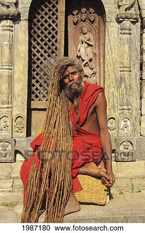Stock Image - Nepal, Kathmandu, Pashupatinath Temple, Hindu Holy Man Sitting On Stairs Wearing Red Robe, Long Dreadlocks.. Fotosearch