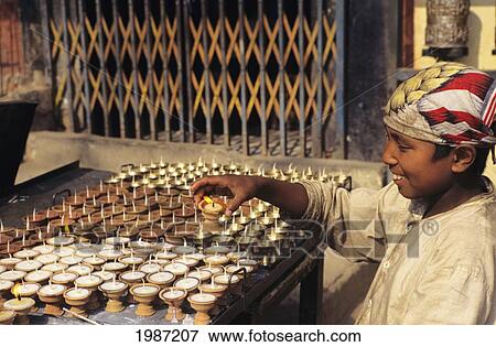 Stock Photo - Nepal, Kathmandu, Smiling Local Boy Lighting Religious Candles, View From Side.. Fotosearch