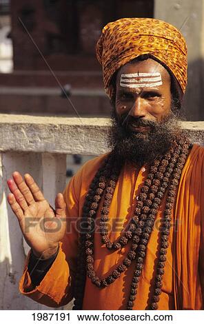 Stock Image - Nepal, Kathmandu Valley, Hindu Holy Man In Orange Robe And Turban, Smiling And Gesturing With Hand. Editorial Use Only.. Fotosearch