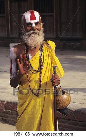Stock Photograph - Nepal, Kathmandu Valley, Senior Hindu Holy Man Standing On Roadside In Colorful Apparel, Gesturing With Hand. Editorial Use Only.. Fotosearch
