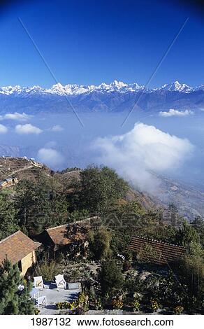 Stock Image - Nepal, Overview of Fort Hotel on hillside and clouds with himalayan mountains in background; Nagarkot. Fotosearch
