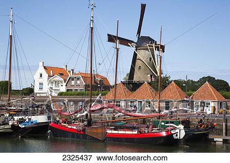 Stock Photo - Netherlands, Zealand, Boats docked in the harbor with a windmill in the background; Zierikzee. Fotosearch