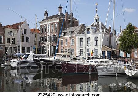 Stock Image - Netherlands, Zealand, Boats in harbour and buildings by waterfront; Goes. Fotosearch