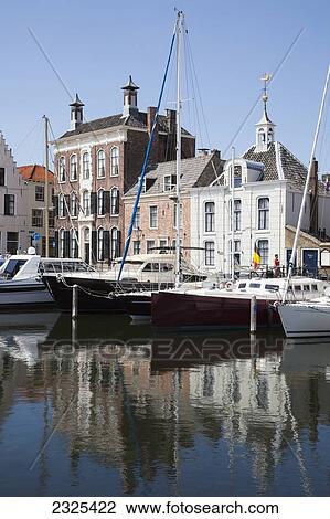 Stock Image - Netherlands, Zealand, Boats in harbour and buildings by waterfront; Goes. Fotosearch