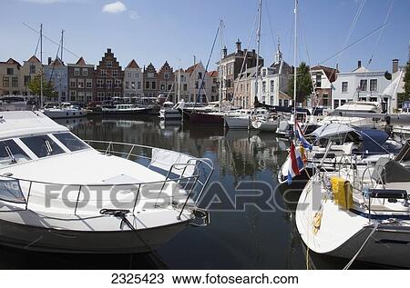Stock Image - Netherlands, Zealand, Boats in harbour and buildings by waterfront; Goes. Fotosearch