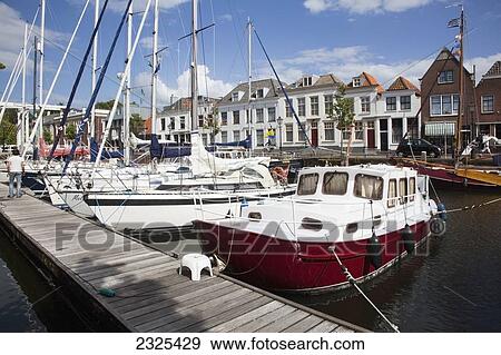 Stock Photo - Netherlands, Zealand, Boats in harbour along wooden pier and buildings along waterfront; Goes. Fotosearch