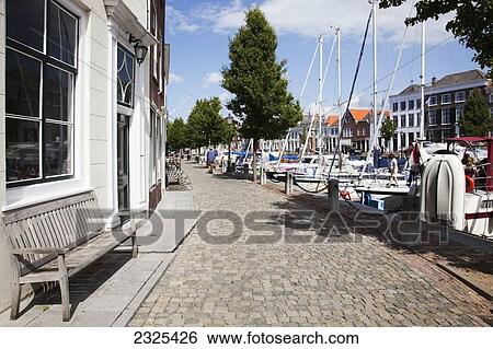 Stock Photograph - Netherlands, Zealand, Promenade along waterfront with boats in harbour; Goes. Fotosearch