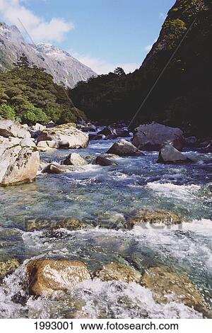 Stock Image - New Zealand, Fiordlands National Park, Stream Bubbling Through A Valley Of Majestic Mountains.. Fotosearch