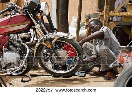 Stock Photo - Niger, Air Region, Housa mechanic fixing motorbike in back street; Agadez. Fotosearch