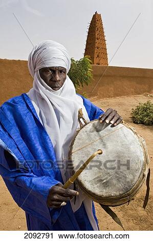 Stock Image - Niger, Sahara Desert, Agadez Region, Tuareg drummer standing next to Agadez Grand Mosque; Agadez. Fotosearch