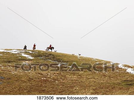 Stock Photograph - Northumberland, England; A Group Of People Riding Horses On The Top Of A Hill With Traces Of Snow On It. Fotosearch