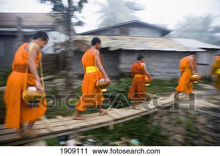 Stock Image - Novice Monks Out In Early Morning Collecting Alms At Wat Naluang, Luang Prabang, Northern Laos. Fotosearch