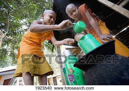 Stock Image - Novice Monks Preparing Wild Root And Herbal Tea At Wat Naluang, Luang Prabang, Northern Laos. Fotosearch