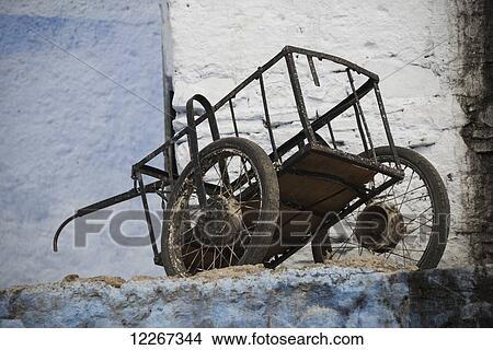 Picture - Old cart resting amongst faded blue and white painted buildings; Chefchaouen, Morocco. Fotosearch