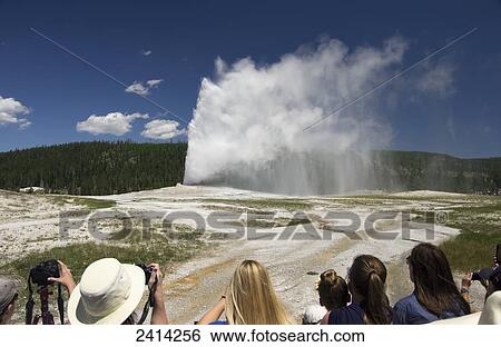Stock Photograph - Old Faithful blows as tourists take photos of the geyser, Yellowstone National Park; Wyoming, United States of America. Fotosearch