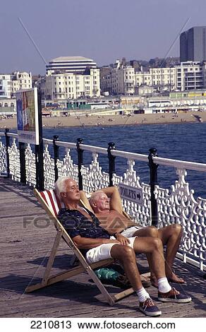 Stock Image - Old Men Soaking Up The Sun In Deckchairs On The Pier, Brighton, East Sussex, England. Fotosearch