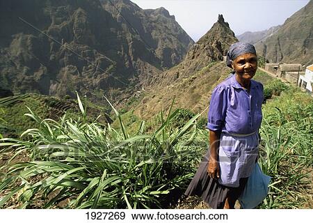 Stock Photo - Old Woman In Front Of Mountain, Portrait; Ribeira Do Paul, Santo Antao Island, Portugal. Fotosearch