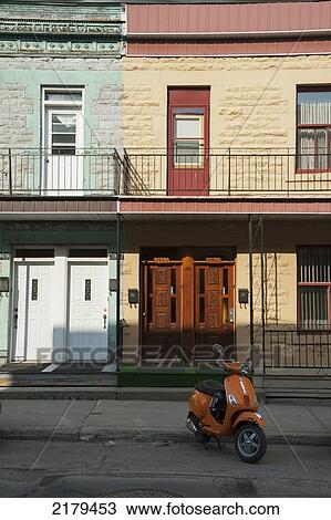 Stock Image - Orange Motor Scooter Parked In Front Of A Residential Building; Montreal Quebec Canada. Fotosearch