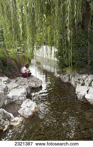 Stock Photo - Oregon, Portland, Chinese Gardens, Young Girl Sitting On Rocks Near Stream.. Fotosearch