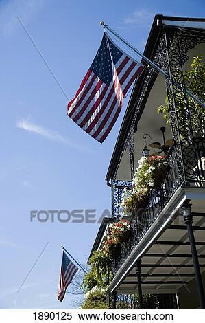 Stock Photography - Ornate Wrought Iron Balcony With Flower Hanging Baskets And Two Us Flags Flying. Fotosearch