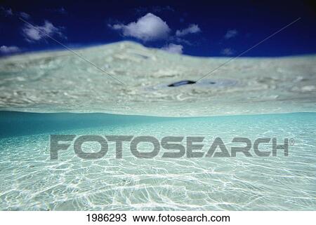 Stock Image - Over/Under View Of Blue Sky, Ocean Water Textures And Sandy Bottom.. Fotosearch