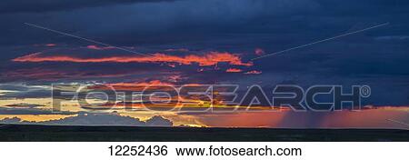Stock Photograph - Panoramic vew of sunset lit clouds and a rain shower over Grasslands National Park; Saskatchewan, Canada. Fotosearch