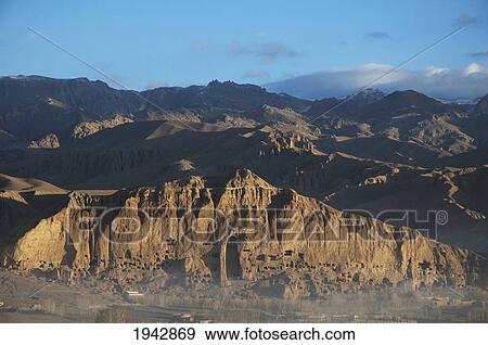 Stock Photo - Panoramic View Of Bamiyan And The Escarpment With Hundreds Of Caves And The Niche That Contained The Small Buddha Statue Destroyed By The Taliban In 2001, Bamian Province, Afghanistan. Fotosearch