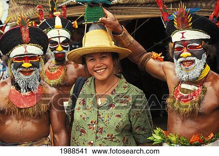 Stock Image - Papua New Guinea, Three Native Men With Traditional Face Paint Pose With Tourist No Model Release. Fotosearch