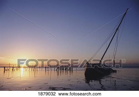 Stock Image - Partly Submerged And Keeling Sail Boat In Silhouette At Sunset. Fotosearch