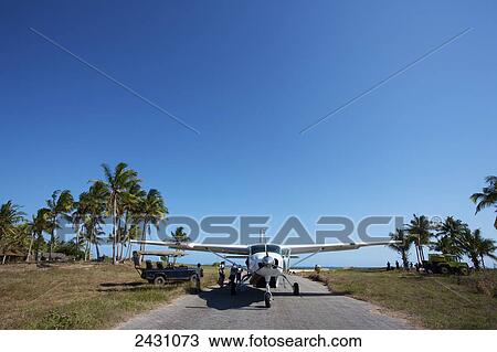 Stock Image - Passengers loading into a white plane sitting on a landing strip; Vamizi Island, Mozambique. Fotosearch